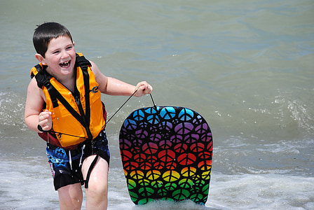 boy wearing orange life vest holding multicolored knee board thumbnail