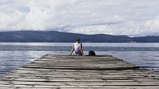 Person Sitting on Brown Wooden Dock Under Cloudy Blue Sky thumbnail