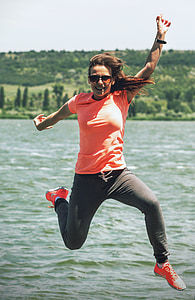 photo of woman jumping near body of water during daytime thumbnail
