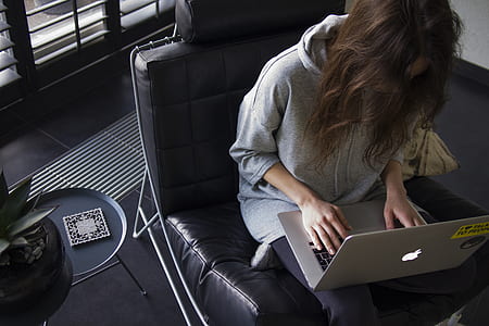 woman in gray pullover hoodie using MacBook seating on black sofa chair thumbnail