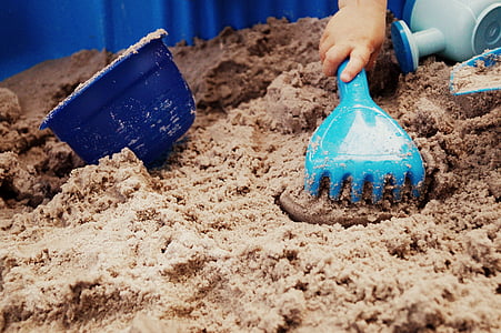 person holding blue plastic sand rake beside bucket on white sand thumbnail