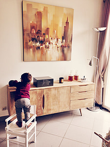 child standing on white wooden armchair in front of wooden sideboard thumbnail