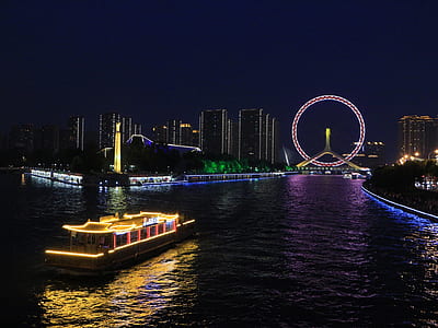 cruiser boat with lights leading to Ferris wheel during night thumbnail
