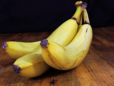 three yellow bananas on brown wooden surface thumbnail