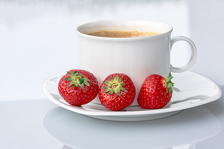 three strawberries on saucer beside white ceramic mug filled with coffee thumbnail