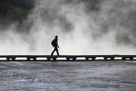 man in backpack walking on dock surrounded by body of water thumbnail