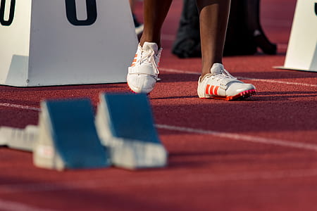 person wearing white-and-orange adidas running shoes on track and field thumbnail