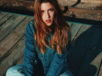 woman wearing blue chambray jacket sitting cross-legged on plankboard floor thumbnail