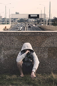 man in grey zip-up hoodie sitting behind grey concrete wall thumbnail