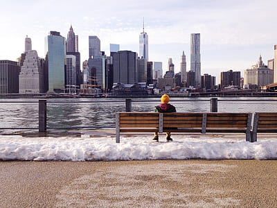 person sitting in bench facing to body of water and buildings thumbnail