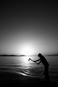 silhouette photo of person holding axe on body of water thumbnail