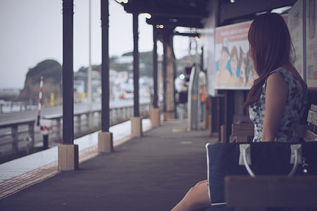 selective focus photography of woman wearing white and gray digital camouflage sleeveless mini dress sitting on brown wooden bench thumbnail