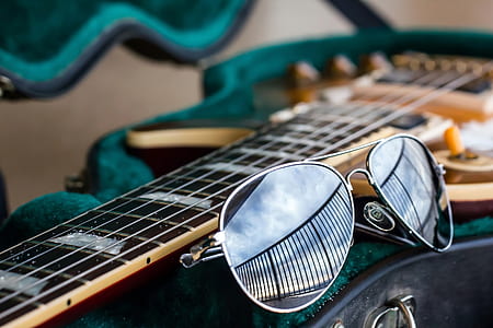 gray framed aviator-style sunglasses beside brown guitar thumbnail