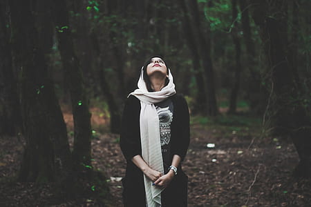 woman wearing beige scarf surrounded by trees while looking up thumbnail