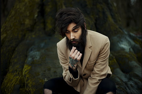 man in brown coat sitting on rock formation thumbnail