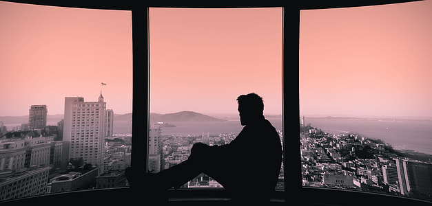 silhouette photo of man sitting beside the glass window thumbnail