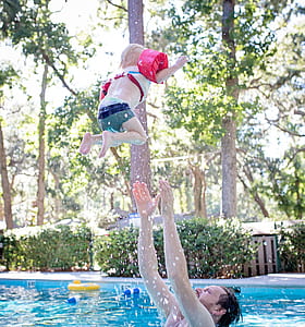 Photography of Man on Swimming Pool Tossing Toddler Above Pool thumbnail