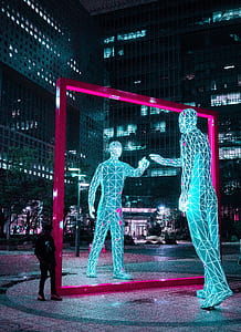 man standing beside tall square purple mirror lighted statue during nighttime thumbnail