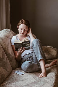woman sitting on gray couch while reading a book thumbnail