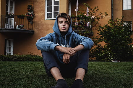 man sits on green grass in front of brown concrete building during daytime thumbnail
