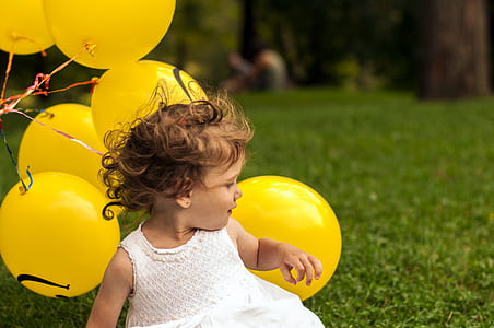 toddler's wearing white sleeveless dress with balloons on back during daytime thumbnail