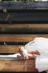 woman in white wedding dress and cork stilettos lying on wooden bench thumbnail