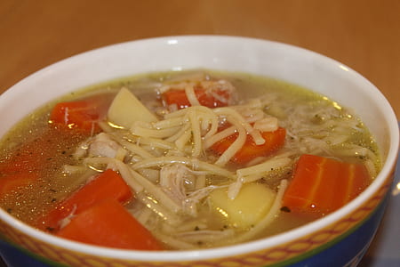 cooked dish with slices of carrots in round white and multicolored ceramic bowl on brown surface thumbnail