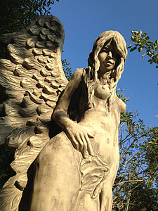 white statue of female angel surrounded by trees under blue sky during daytime thumbnail