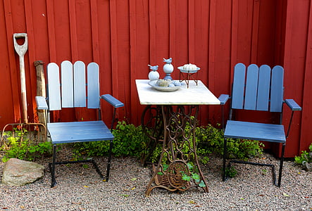 square white table between blue armchairs beside red wooden fence thumbnail