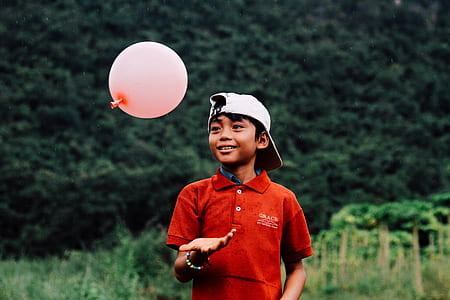 boy playing pink balloon on grass field at daytime thumbnail