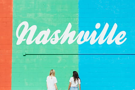 two women in white shirts in front of green and blue wall thumbnail