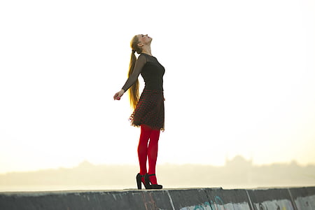 woman wearing black dress and red stockings standing on concrete platform during daytime thumbnail
