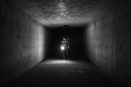 grayscale photo of man holding lamp inside a tunnel thumbnail