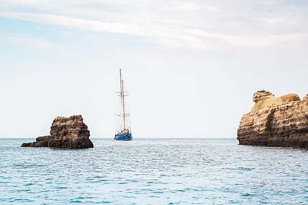 blue ship heading towards rock formation thumbnail