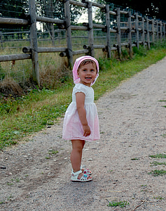 toddler in white and pink dress on brown pathway beside brown fence thumbnail