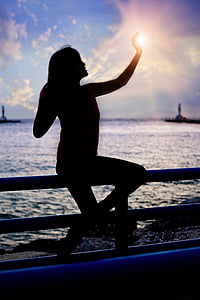 silhouette of person sitting on fence near body of water thumbnail