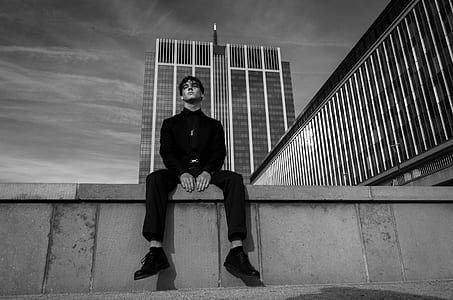grayscale photo of man sitting near building thumbnail