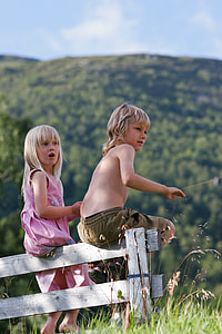 boy and girl sitting on white wooden fence near mountains thumbnail