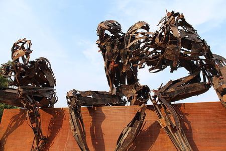 three metal robots statues sitting on brown bench thumbnail