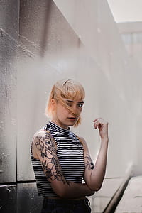 woman black and white striped sleeveless turtleneck shirt with flower arm tattoo taking photo beside wall at daytime thumbnail