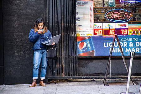 Woman in Blue Jeans Holding Macbook Pro Standing Against Black Wall thumbnail