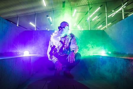 man squatting in between concrete walls while smoking inside lighted room thumbnail