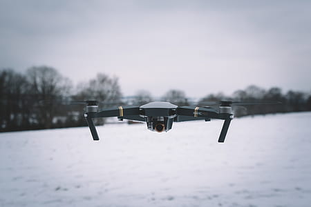 shallow focus photography of black and white drone flying above snowy ground thumbnail