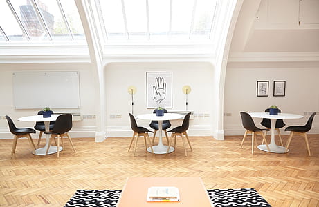 three round white wooden tables with nine black armless chairs thumbnail