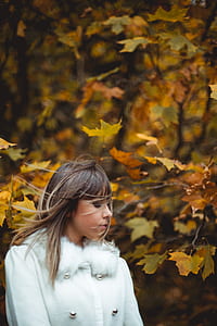 woman wearing coat with hair being blown away next to trees thumbnail