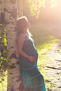 pregnant woman wearing blue maxi dress leaning on tree thumbnail
