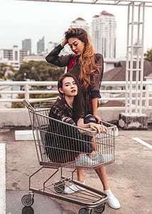 woman sitting on shopping cart beside woman during daytime thumbnail