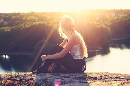 woman sitting on soil near water and green foliage tree during golden hour thumbnail