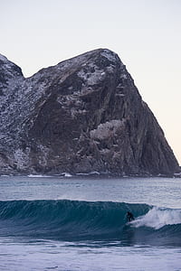 man surfing in sea near rock formation thumbnail