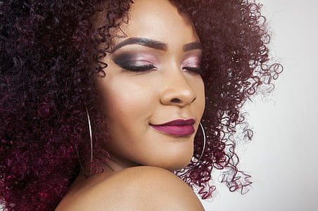 woman with burgundy curly hair wearing smokey pink tone eyeshadow, matte lipstick, and silver-colored hoop earrings thumbnail